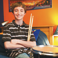 Teenager in black and white striped shirt holding drumsticks, sitting in front of drums